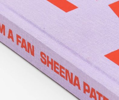 A photograph of the spine of the book "I'm a Fan" by Sheena Patel. The book cover is coloured light purple with orange coloured writing.